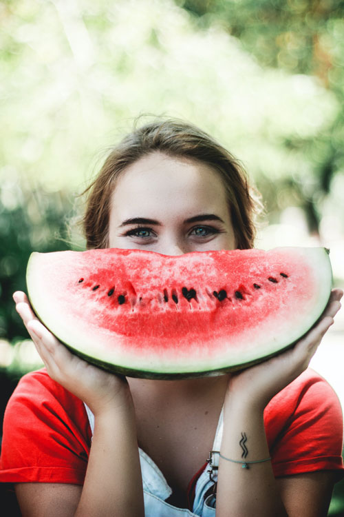 Jeune fille souriante plaçant une grande tranche de pastèque en guise de sourire