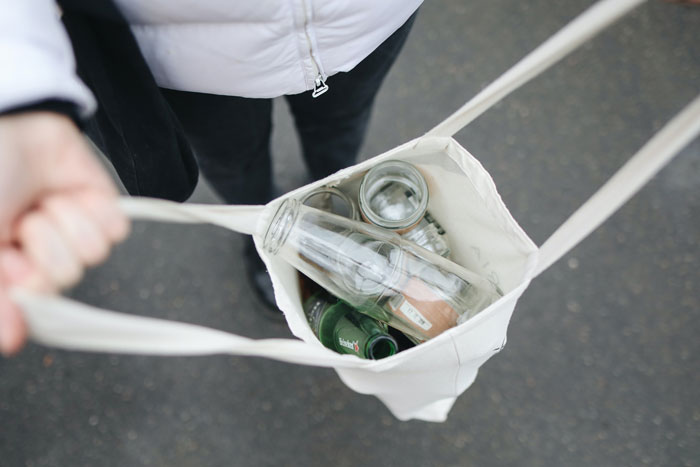 Personne tenant un sac en tissu ouvert contenant des bouteilles en verre vides